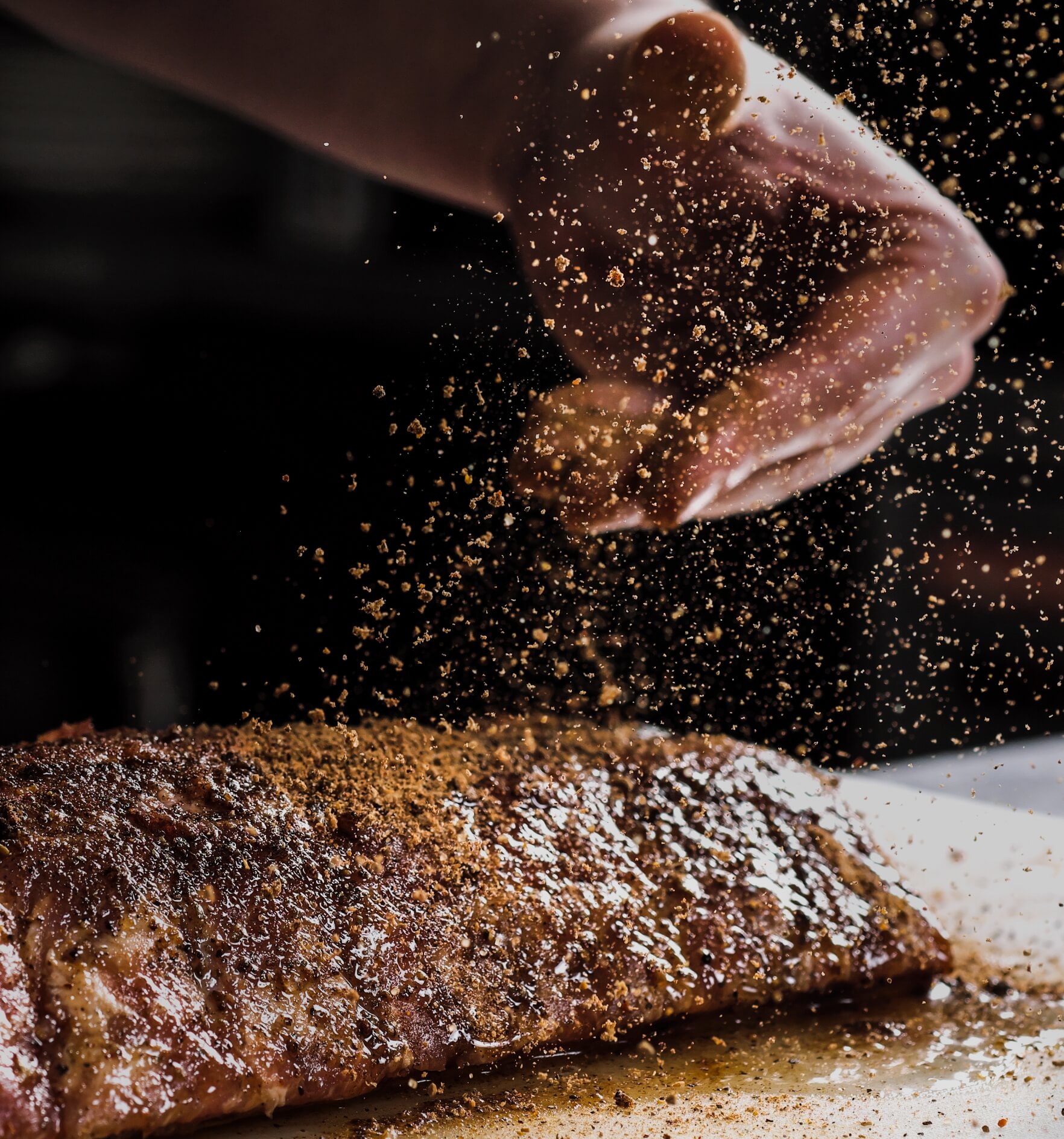 Image showing the hand of a male chef puts salt and spices on a raw piece of meat, beef ribs