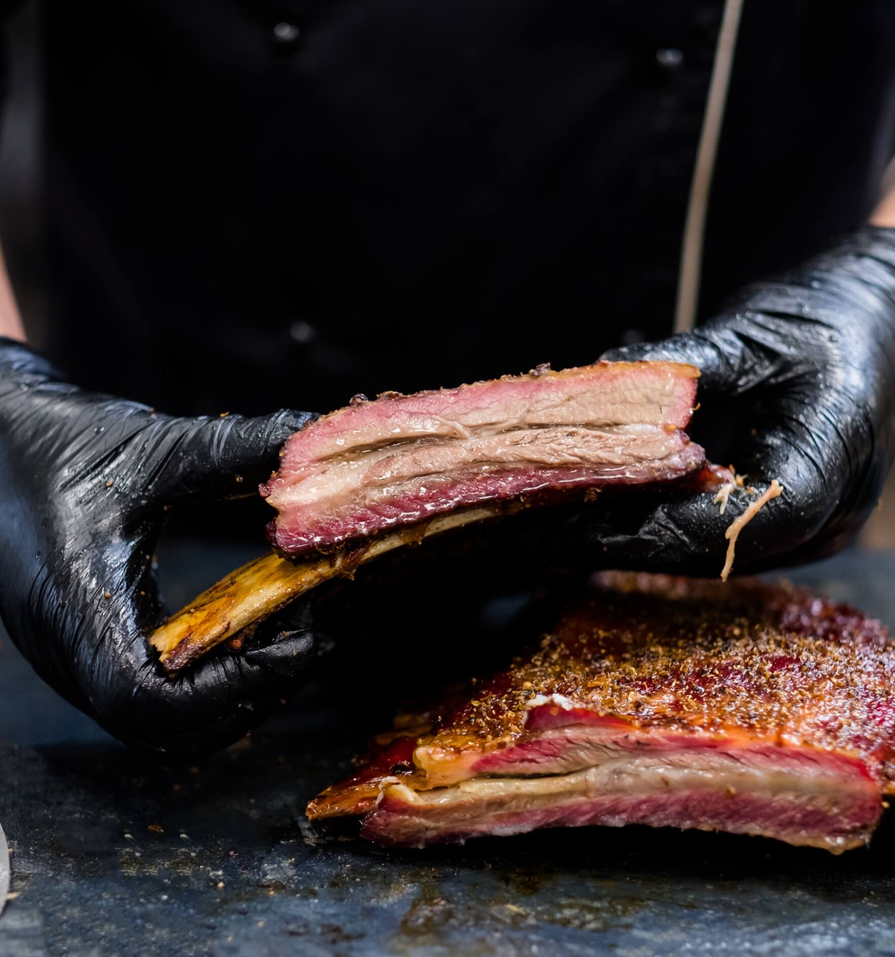 Image showing a closeup of chef hands in black cooking gloves holding smoked beef ribs